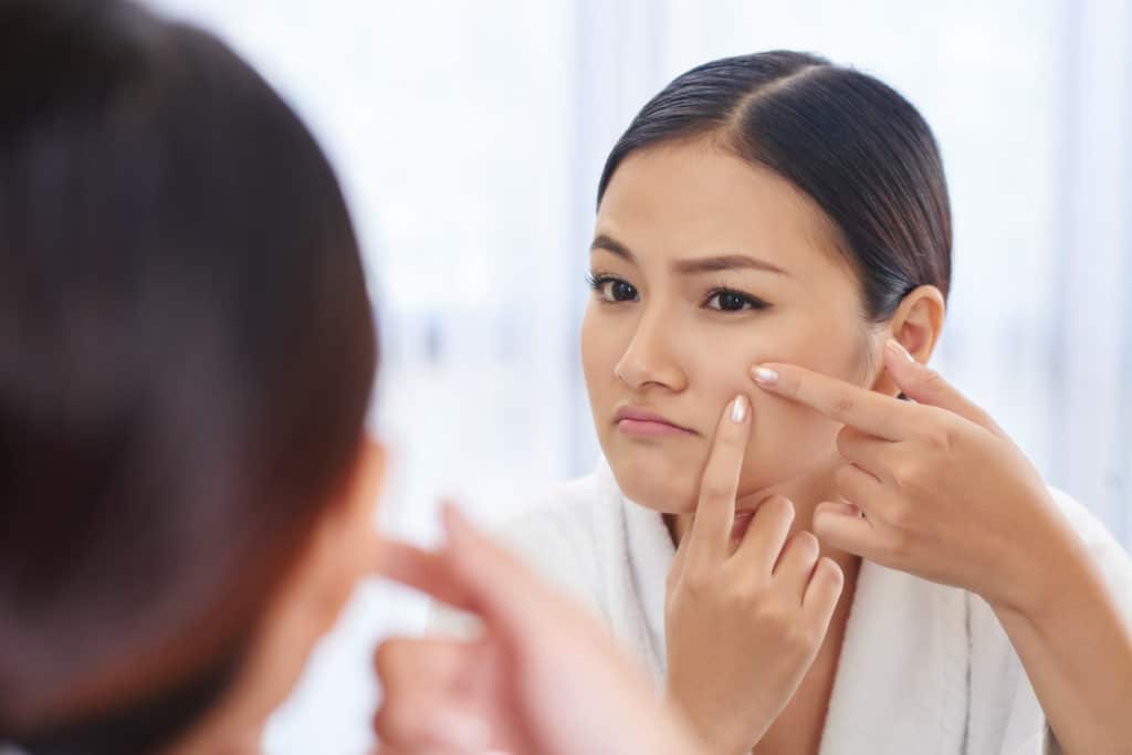 woman checking skin for acne and face blemishes