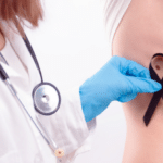 Doctor wearing white coat and stethoscope in gloves putting black ribbon on man’s skin.