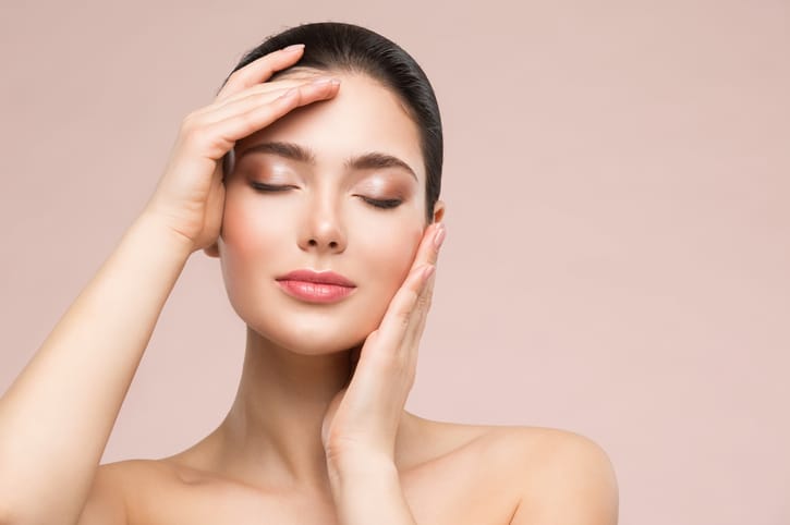 Beautiful Woman Face Skin Care. Natural Make up. Skin Health Treatment. Model massaging Face by Hands. Beige background