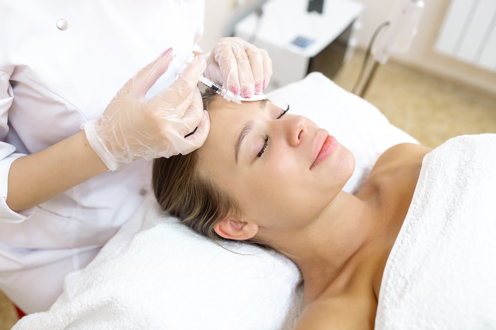 Woman happily receiving Xeomin injections in her forehead to smooth out wrinkles.