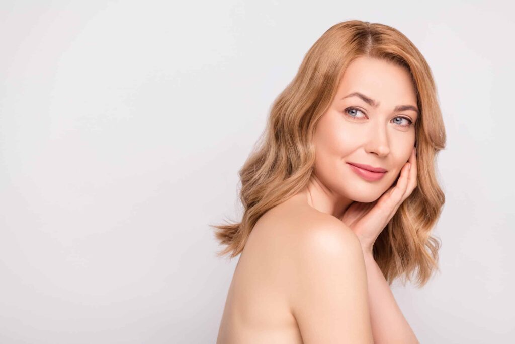 Middle-aged woman smiling and touching her face after getting revitalizing skin treatments